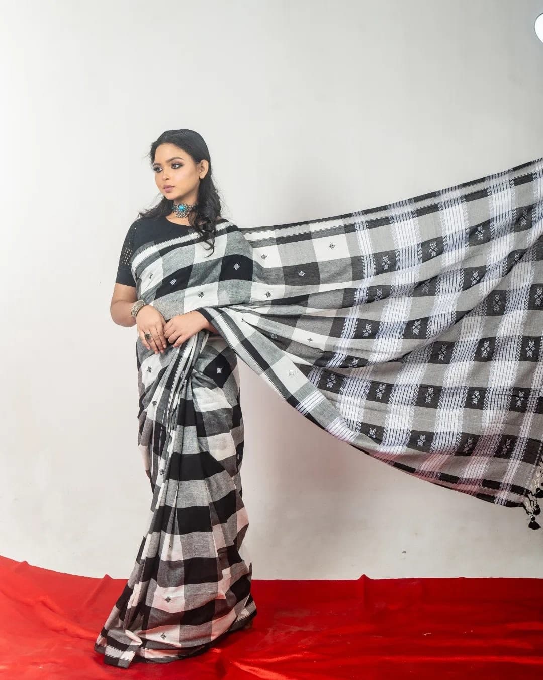 Sanjana Murmu holding the pallu of a black and white checked saree wide across the frame.