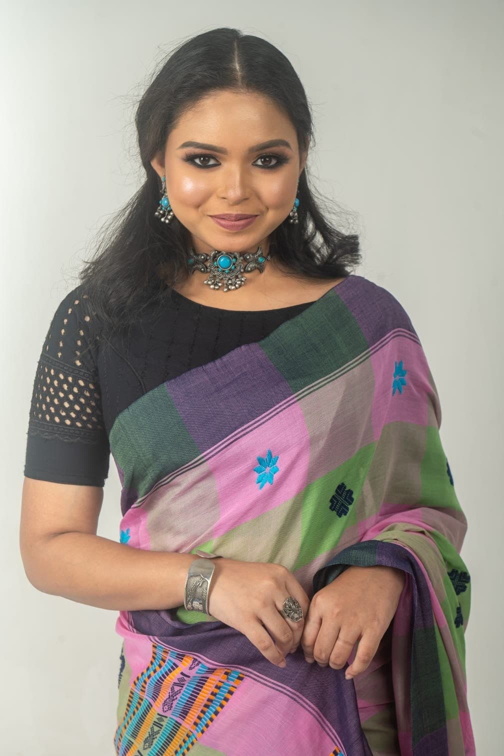 Sanjana Murmu facing the camera in a pink and green handloom saree with a turquoise necklace.