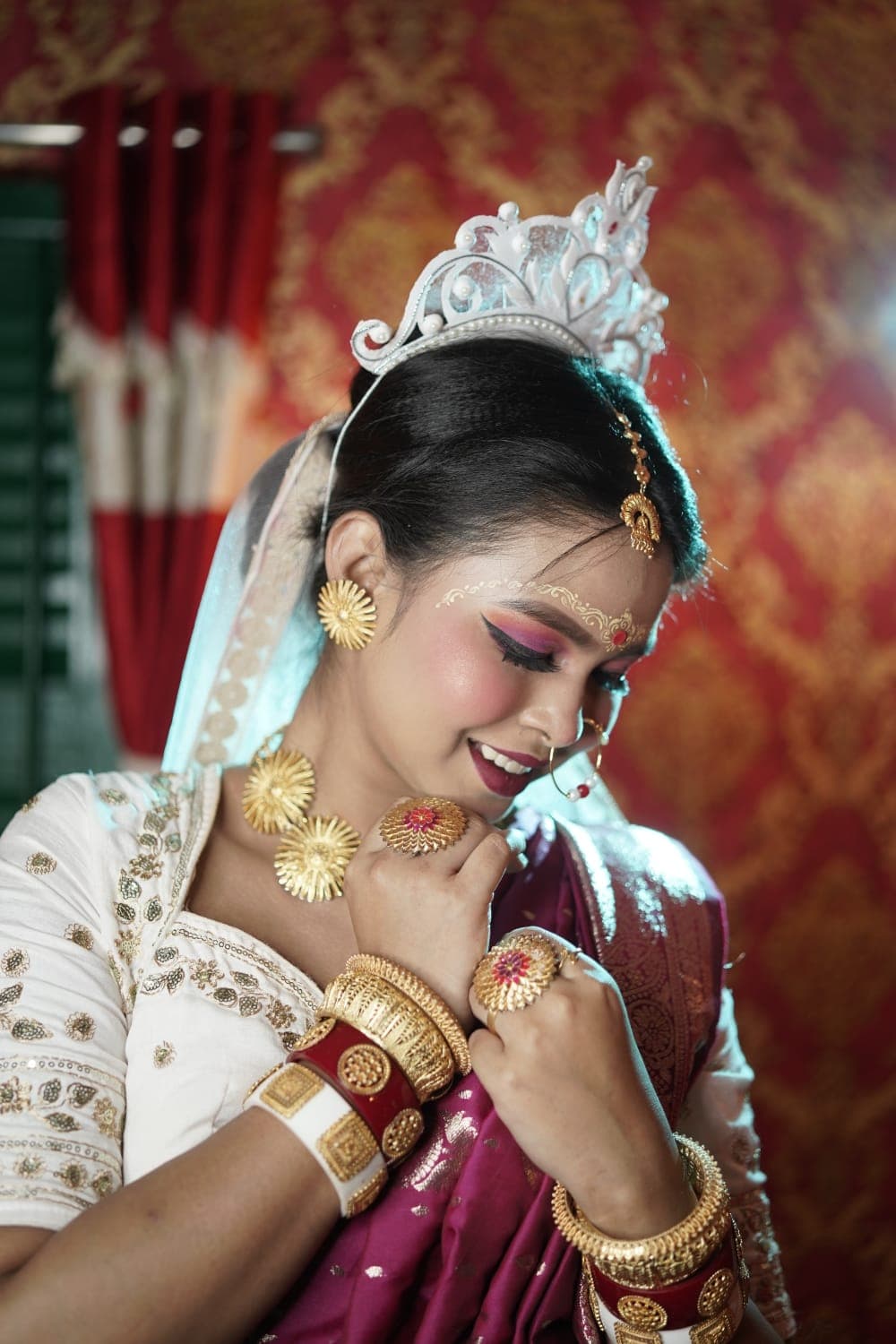 Sanjana Murmu in a silver mukut and magenta saree, head lowered, gold sunburst necklace at her throat.