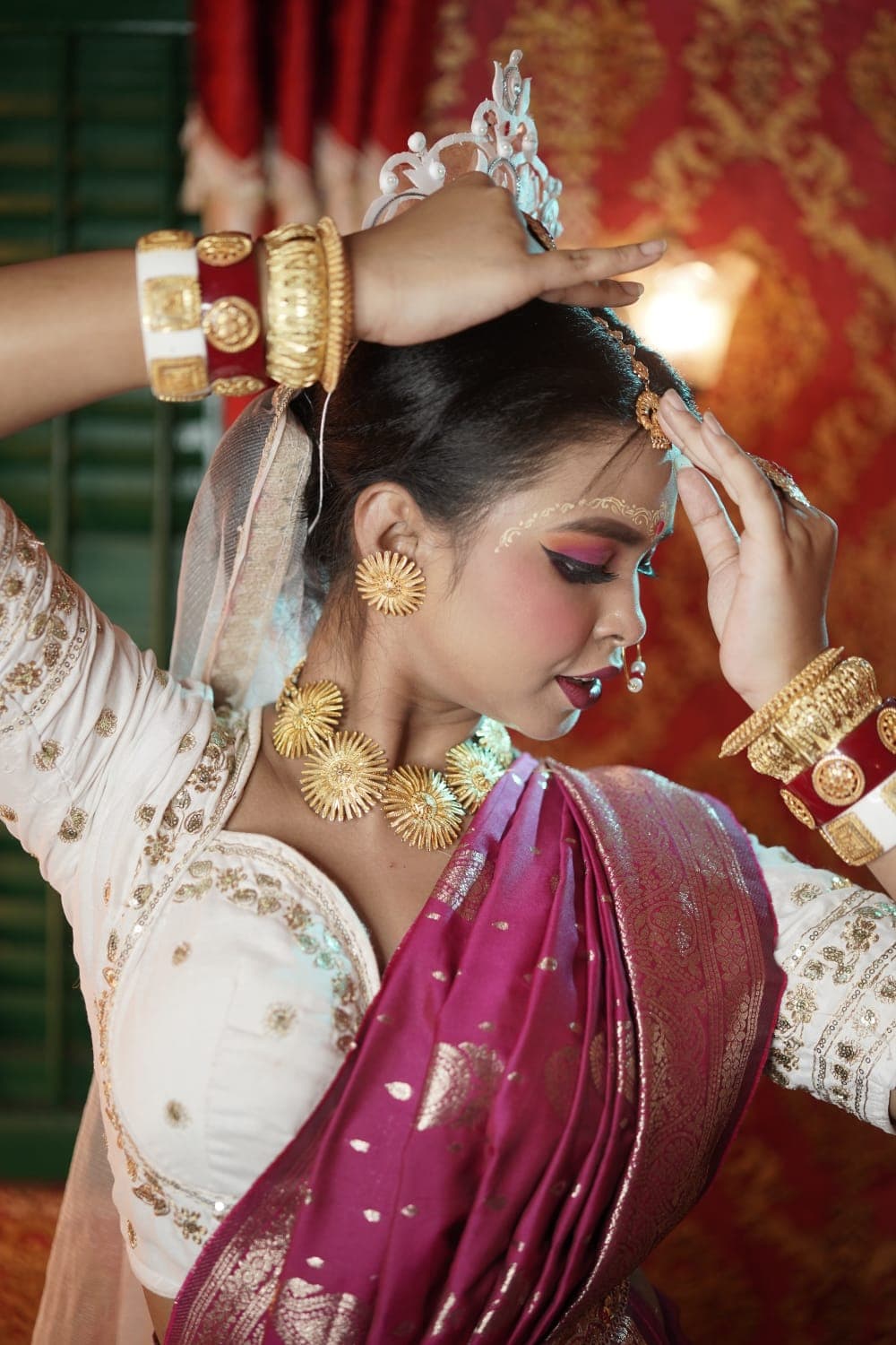 Sanjana Murmu with both hands lifted to her silver mukut, gold bangles stacked along her forearms.