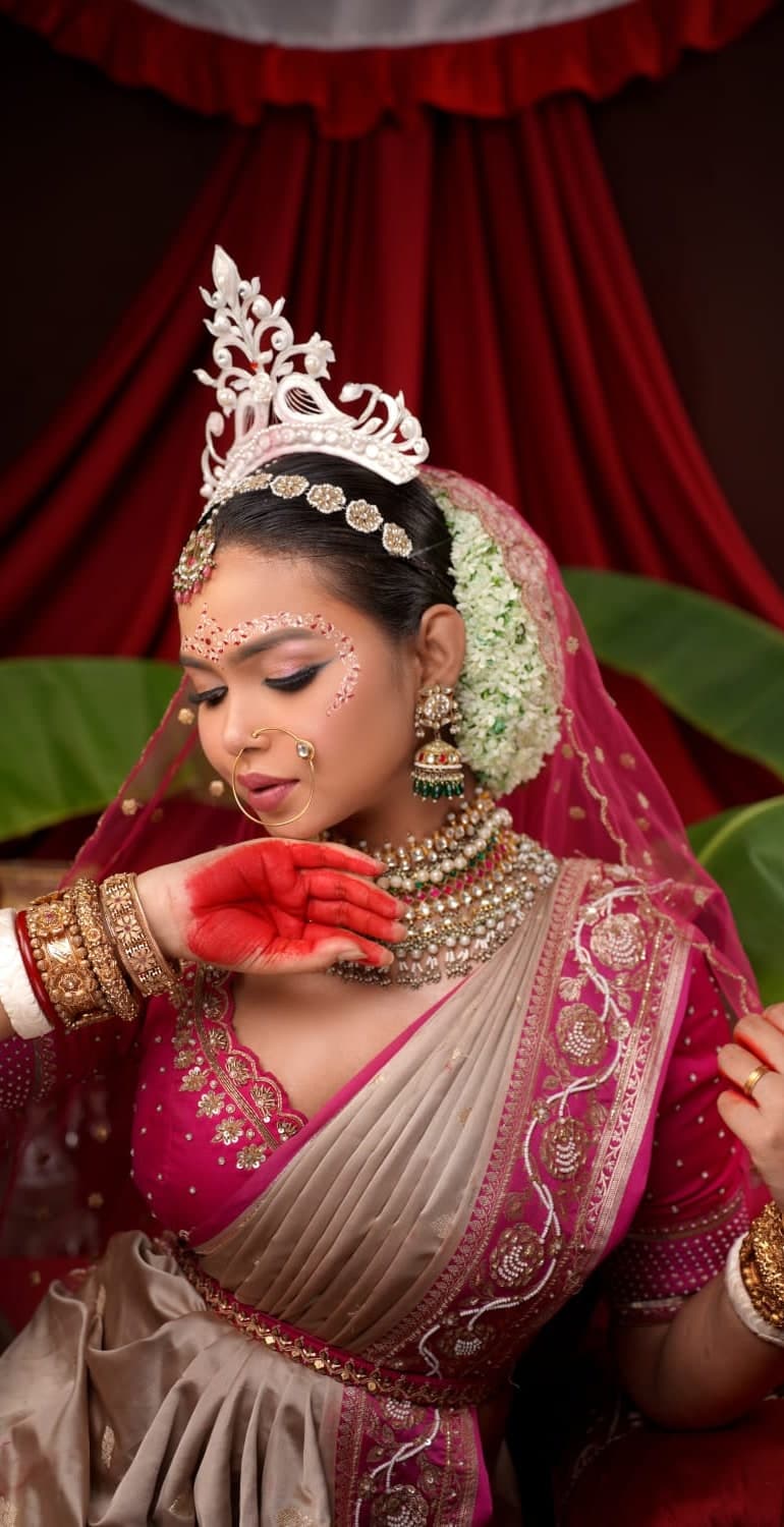 Sanjana Murmu with mehndi-red palms raised, in a magenta bridal saree and white crown.