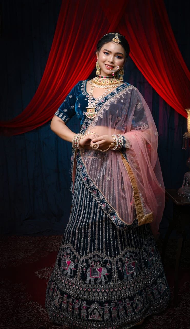 Sanjana Murmu standing full length in a navy velvet lehenga with elephant embroidery, red curtain behind her.