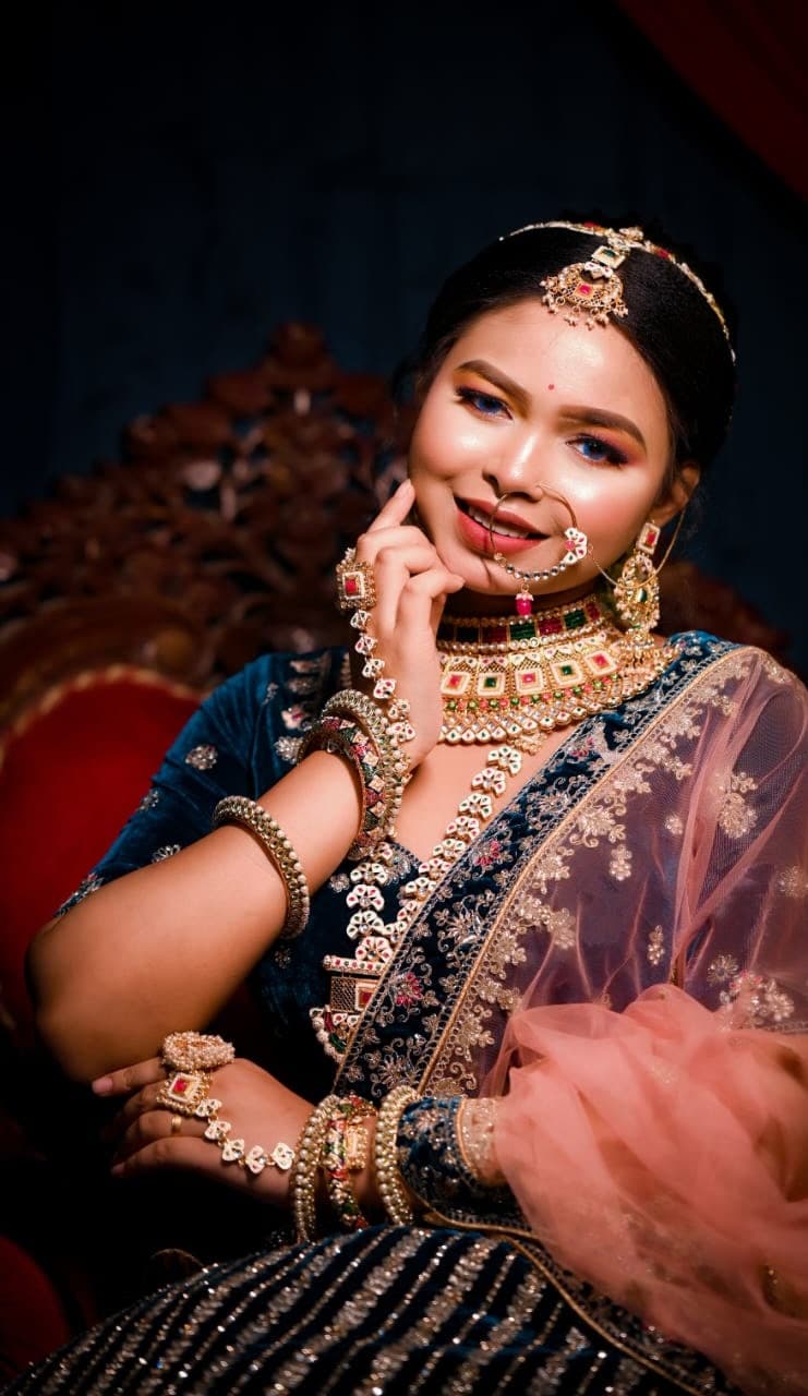 Sanjana Murmu smiling with her hand at her chin, kundan choker and blush dupatta against a dark ground.