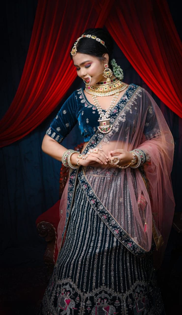 Sanjana Murmu looking down, hands together, navy lehenga and blush dupatta lit from one side.