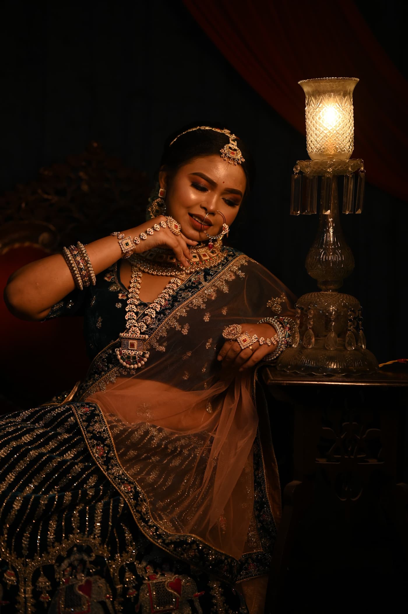 Sanjana Murmu seated in a navy sequinned lehenga beside a lit glass lantern, the room falling away into darkness.