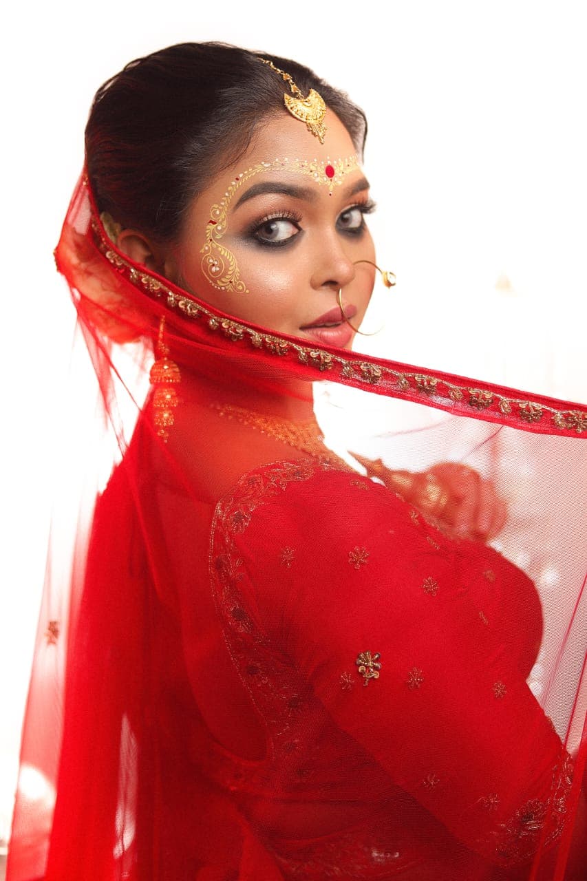 Sanjana Murmu looking back over her shoulder as a red gold-bordered dupatta sweeps across the frame against a bright white background.